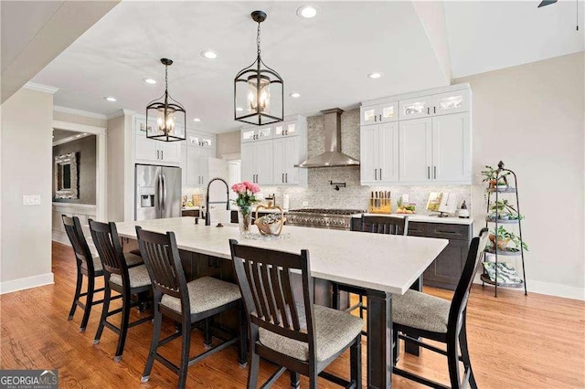 kitchen featuring a large island, wall chimney range hood, white cabinetry, stainless steel fridge with ice dispenser, and decorative light fixtures