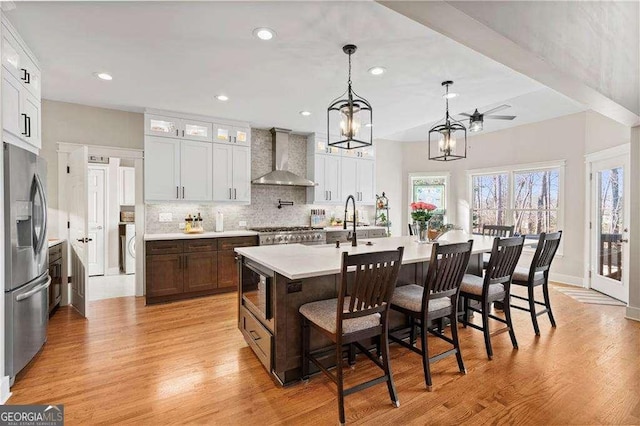 kitchen featuring wall chimney exhaust hood, a kitchen breakfast bar, stainless steel appliances, a kitchen island with sink, and white cabinets