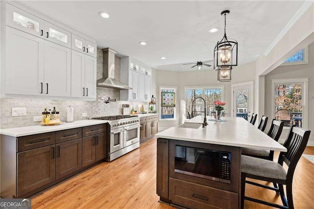 kitchen with built in microwave, white cabinetry, sink, double oven range, and wall chimney exhaust hood