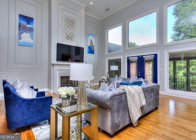 living room featuring a high ceiling, ornamental molding, light wood-type flooring, and french doors