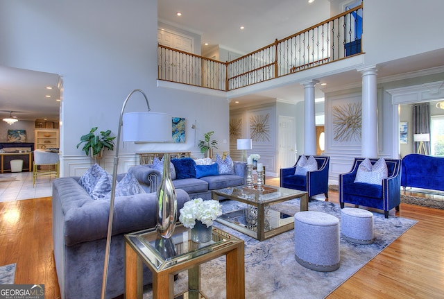 living room with crown molding, wood-type flooring, plenty of natural light, decorative columns, and a high ceiling