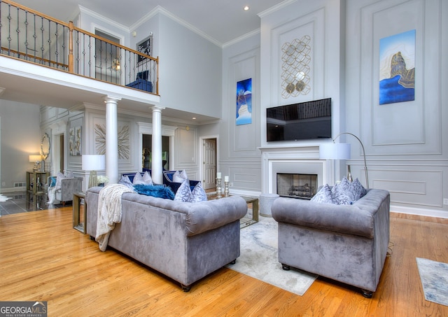 living room with crown molding, light hardwood / wood-style floors, decorative columns, and a high ceiling