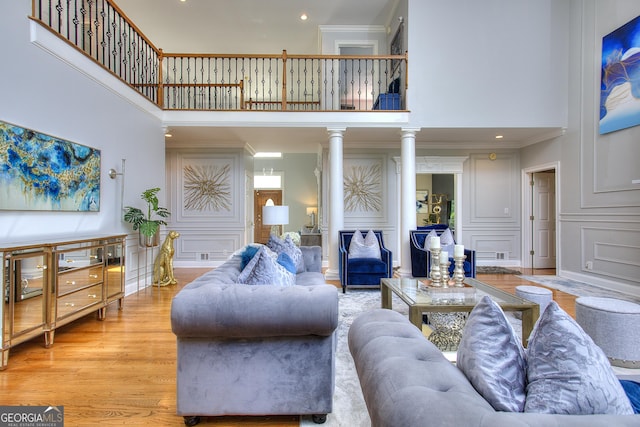 living room with crown molding, a towering ceiling, light hardwood / wood-style flooring, and ornate columns