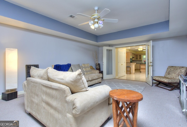 carpeted living room with a raised ceiling and ceiling fan