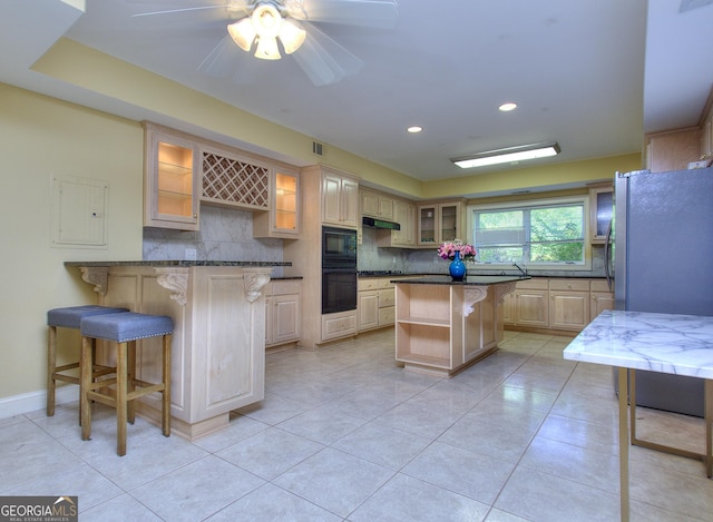 kitchen with a kitchen bar, light tile patterned floors, a kitchen island, decorative backsplash, and black appliances