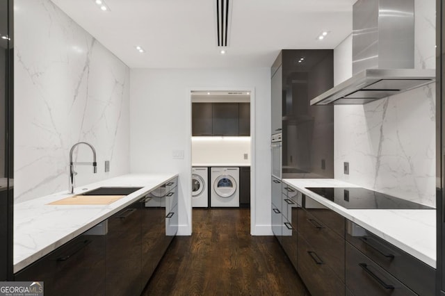 kitchen with sink, dark hardwood / wood-style flooring, black electric cooktop, island exhaust hood, and separate washer and dryer