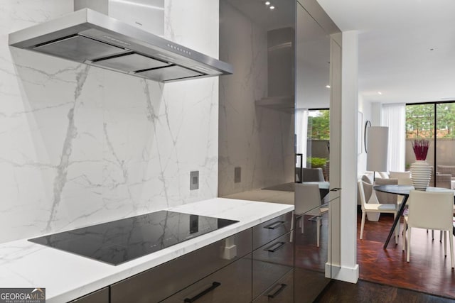 kitchen featuring wall chimney range hood, black electric stovetop, light stone countertops, expansive windows, and dark hardwood / wood-style flooring