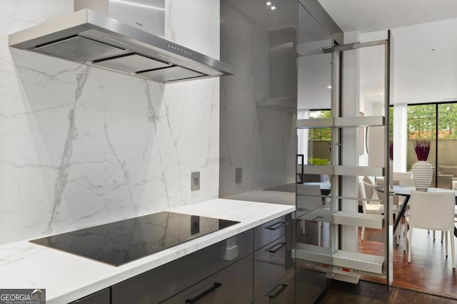 kitchen featuring dark wood-type flooring, light stone counters, black electric cooktop, expansive windows, and range hood