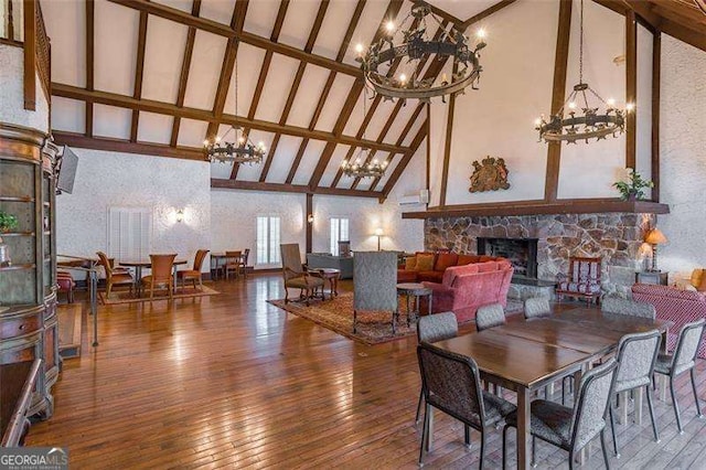 dining area featuring a stone fireplace, beamed ceiling, wood-type flooring, and a notable chandelier