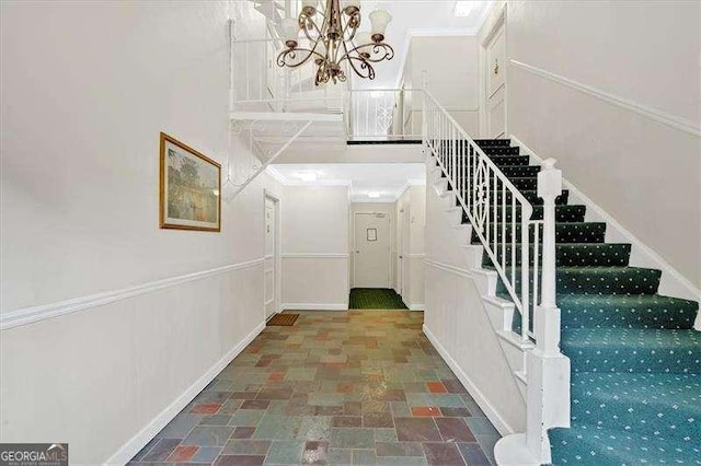 stairway featuring baseboards, stone finish floor, and an inviting chandelier