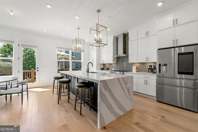 kitchen featuring pendant lighting, white cabinetry, a kitchen island with sink, stainless steel fridge with ice dispenser, and wall chimney exhaust hood