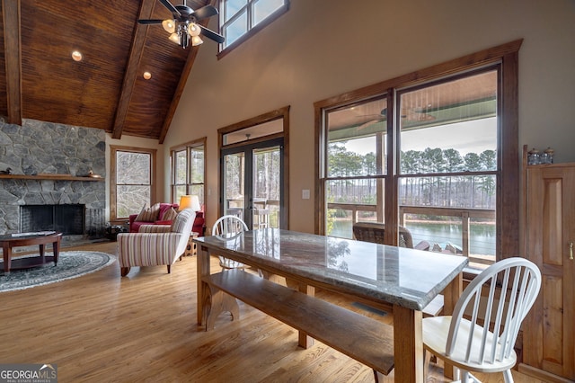 dining space featuring beam ceiling, high vaulted ceiling, wooden ceiling, a fireplace, and light hardwood / wood-style floors