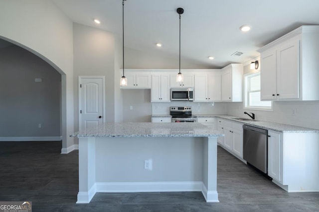 kitchen with light stone counters, hanging light fixtures, a kitchen island, stainless steel appliances, and white cabinets