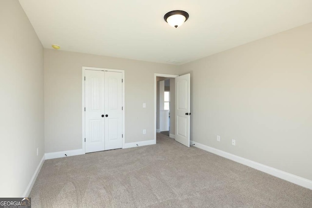 unfurnished bedroom with light colored carpet and a closet