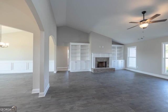 unfurnished living room featuring built in features, dark hardwood / wood-style flooring, a brick fireplace, ceiling fan with notable chandelier, and vaulted ceiling