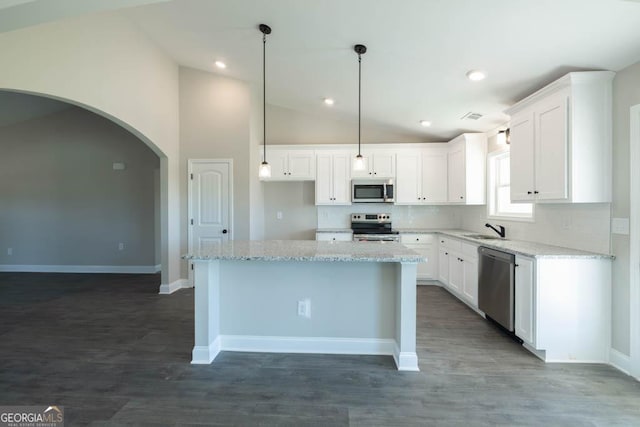 kitchen with a kitchen island, lofted ceiling, white cabinets, stainless steel appliances, and light stone countertops