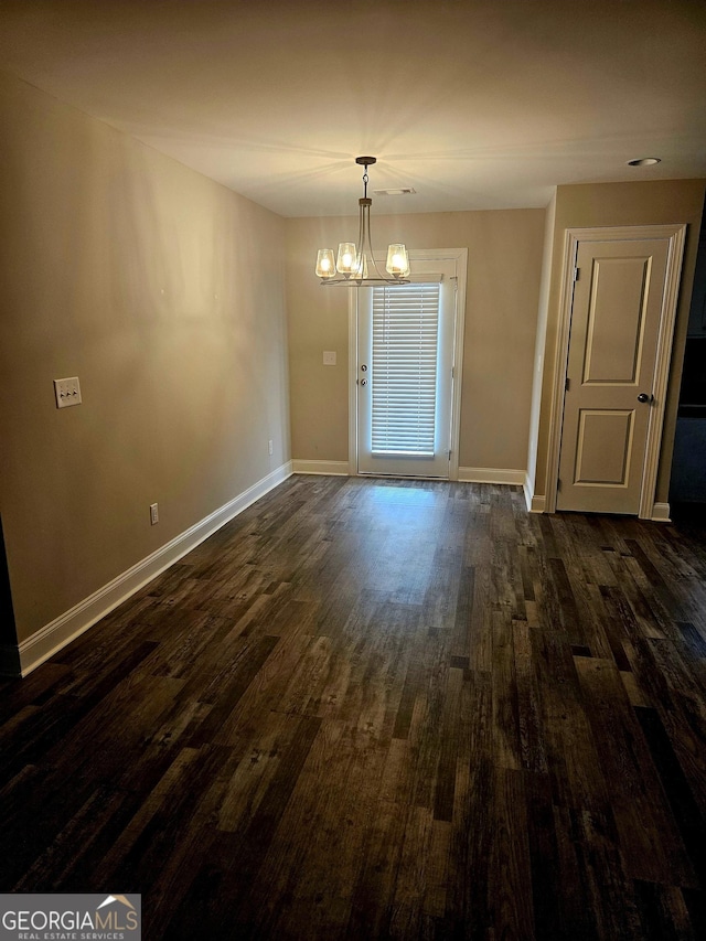 spare room with dark hardwood / wood-style flooring and a notable chandelier