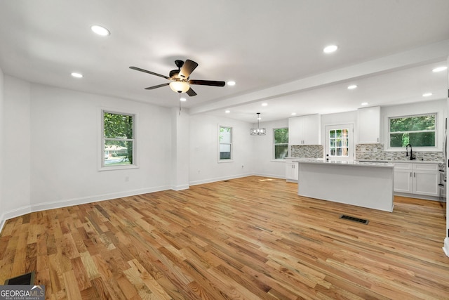 unfurnished living room with sink, plenty of natural light, light hardwood / wood-style floors, and beamed ceiling