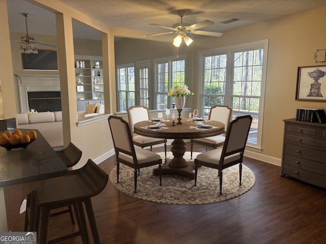 dining room with a wealth of natural light, dark wood-style flooring, visible vents, and a glass covered fireplace