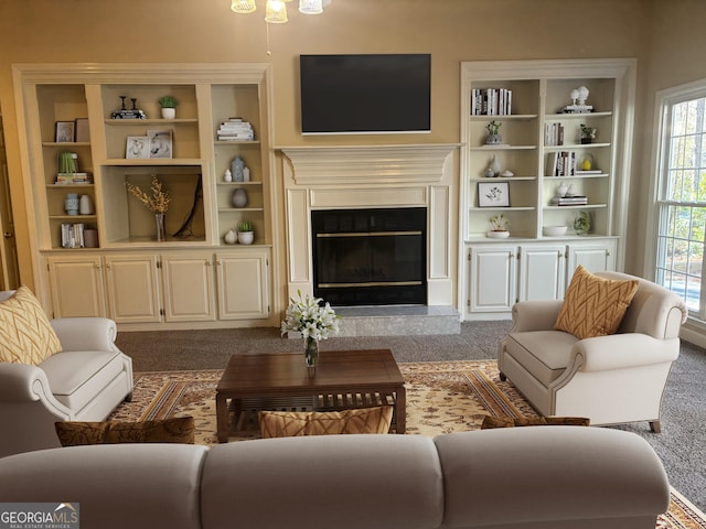 living room with built in shelves, a glass covered fireplace, and dark colored carpet