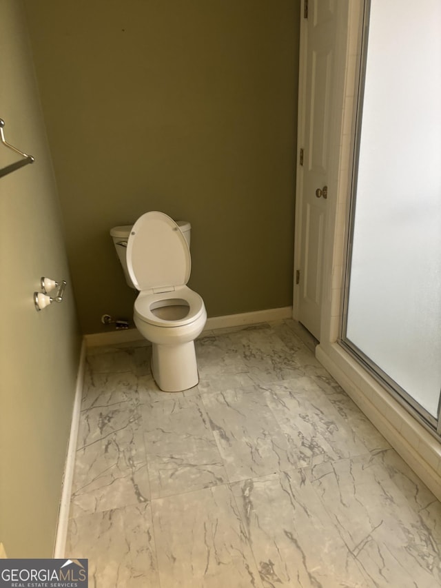 bathroom with marble finish floor, a stall shower, toilet, and baseboards