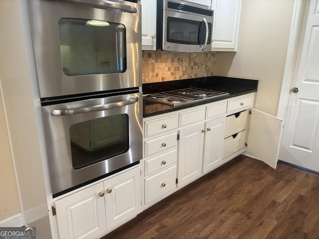 kitchen featuring tasteful backsplash, white cabinets, dark wood finished floors, dark countertops, and appliances with stainless steel finishes