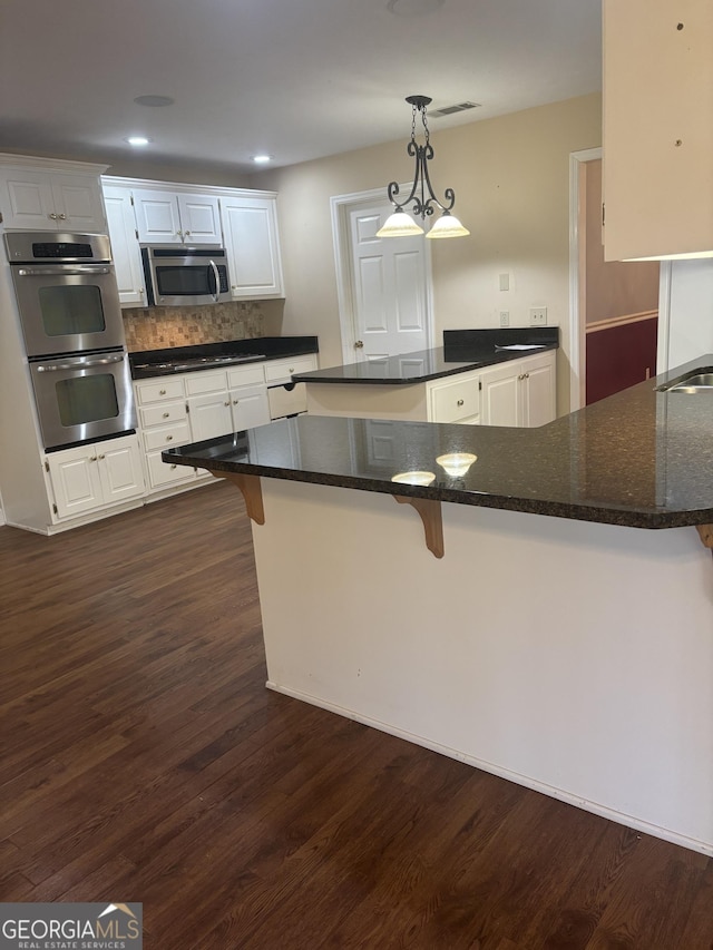 kitchen featuring pendant lighting, a breakfast bar, white cabinetry, backsplash, and stainless steel appliances