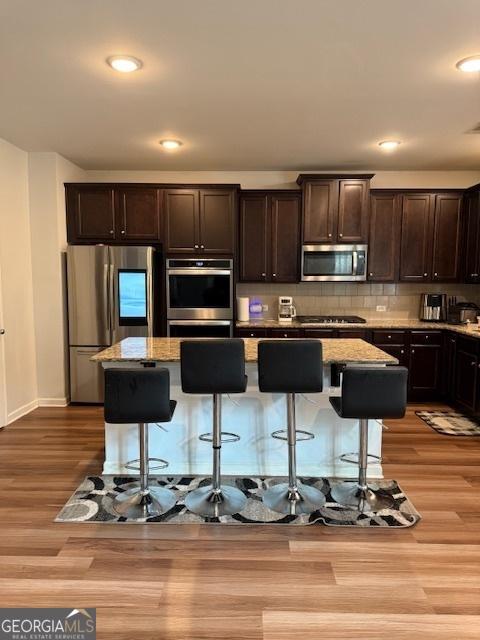 kitchen with a kitchen island, appliances with stainless steel finishes, stone countertops, a breakfast bar, and dark brown cabinetry