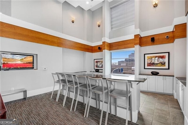 kitchen featuring a kitchen bar, white cabinetry, an island with sink, tile patterned flooring, and a high ceiling