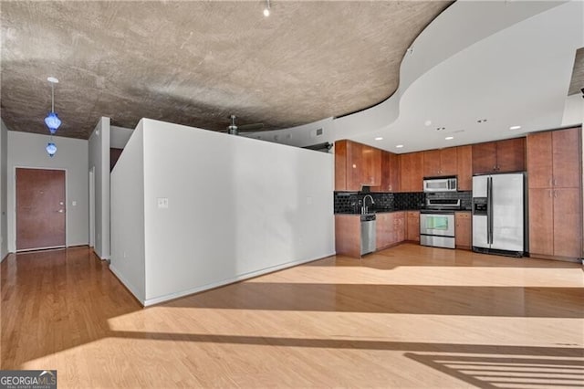 kitchen with appliances with stainless steel finishes, light hardwood / wood-style flooring, and backsplash