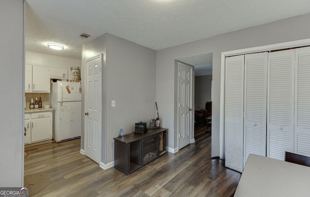 kitchen featuring white refrigerator, a textured ceiling, white cabinets, dark hardwood / wood-style flooring, and decorative backsplash