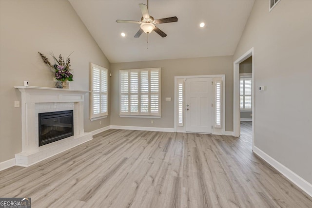 unfurnished living room featuring a brick fireplace, light hardwood / wood-style flooring, high vaulted ceiling, and ceiling fan