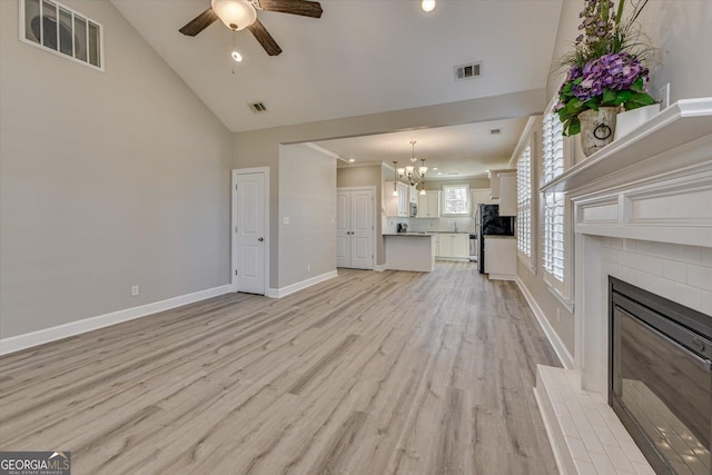 unfurnished living room featuring high vaulted ceiling, ceiling fan with notable chandelier, and light wood-type flooring