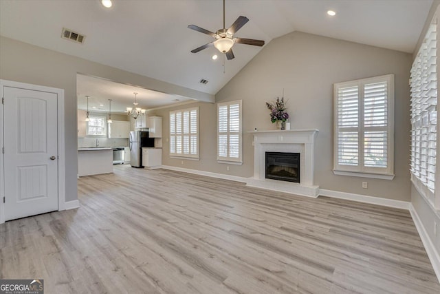 unfurnished living room featuring lofted ceiling, sink, a brick fireplace, light hardwood / wood-style flooring, and ceiling fan with notable chandelier