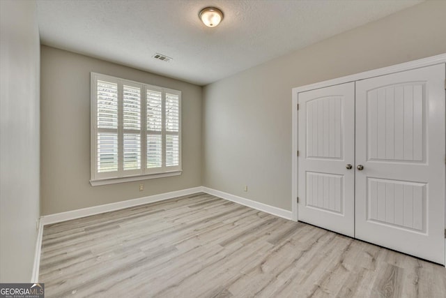 unfurnished bedroom featuring light hardwood / wood-style flooring, a closet, and a textured ceiling