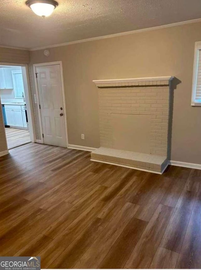 unfurnished room featuring dark wood-type flooring, a fireplace, a textured ceiling, and crown molding