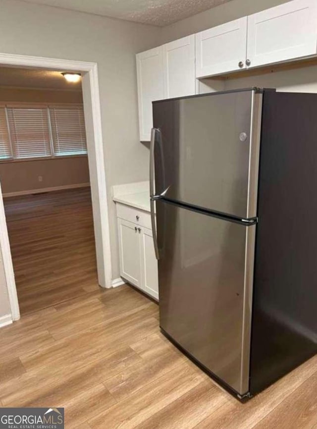 kitchen featuring stainless steel fridge, a textured ceiling, light hardwood / wood-style flooring, and white cabinets