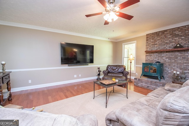 living room featuring hardwood / wood-style floors, ornamental molding, ceiling fan, and a wood stove