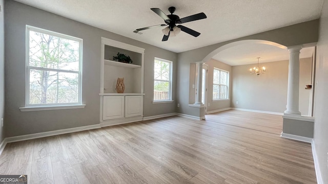 spare room featuring built in shelves, ornate columns, a textured ceiling, light hardwood / wood-style flooring, and ceiling fan with notable chandelier