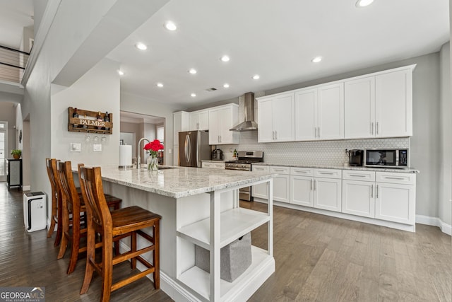 kitchen with sink, a kitchen breakfast bar, stainless steel appliances, white cabinets, and wall chimney exhaust hood