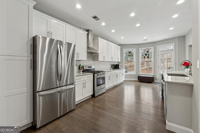 kitchen with sink, wall chimney range hood, stainless steel appliances, light stone countertops, and white cabinets