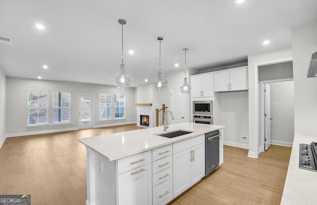 kitchen with a center island with sink, sink, pendant lighting, and white cabinets