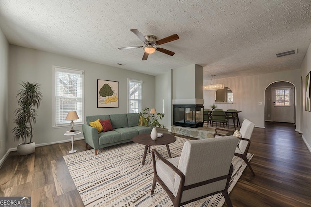 living room featuring dark hardwood / wood-style flooring, a wealth of natural light, ceiling fan, and a multi sided fireplace