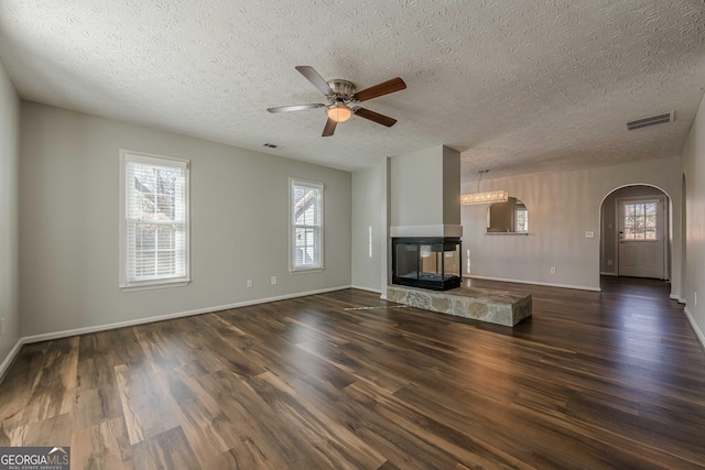 unfurnished living room with ceiling fan, dark wood-type flooring, plenty of natural light, and a multi sided fireplace