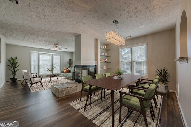 dining room featuring dark hardwood / wood-style flooring, ceiling fan, a textured ceiling, and a multi sided fireplace