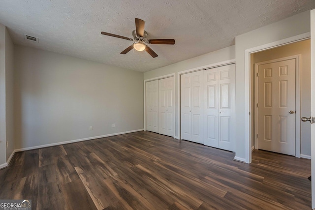 unfurnished bedroom with multiple closets, ceiling fan, dark wood-type flooring, and a textured ceiling