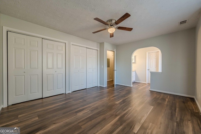 unfurnished bedroom featuring two closets, dark wood-type flooring, and a textured ceiling