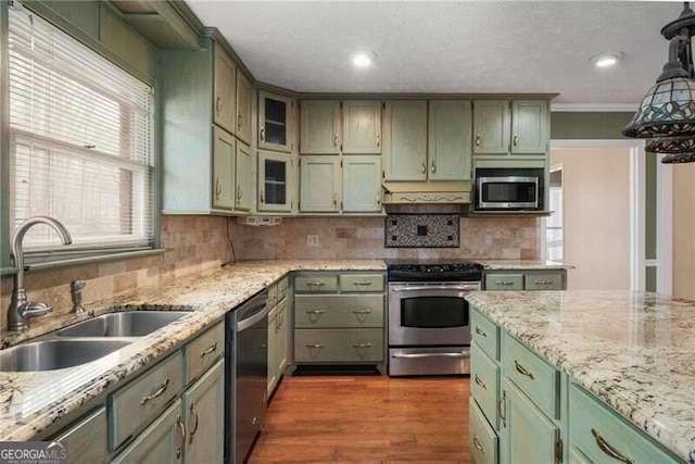 kitchen with light stone counters, sink, stainless steel appliances, and green cabinets