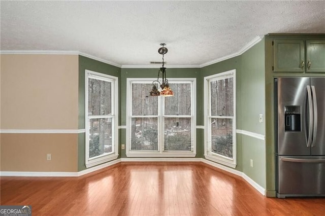 unfurnished dining area featuring ornamental molding, an inviting chandelier, a textured ceiling, and light wood-type flooring