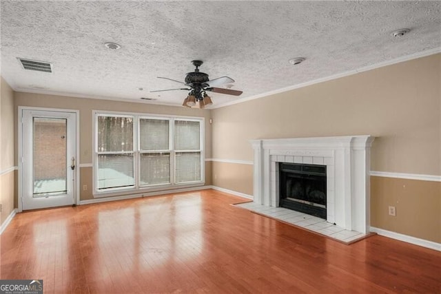 unfurnished living room with a tiled fireplace, ornamental molding, ceiling fan, and light hardwood / wood-style flooring